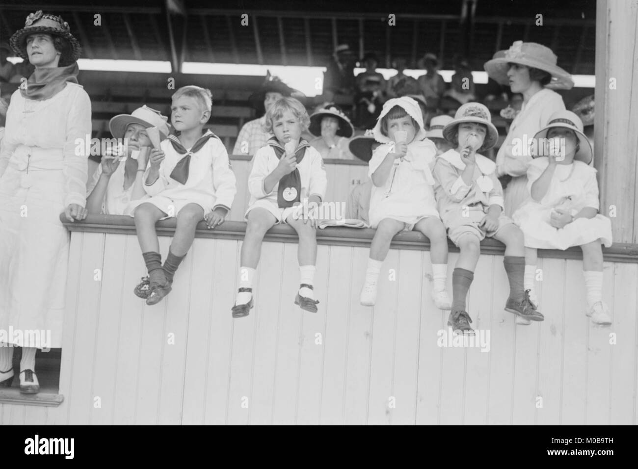 Children sit on wall in front of stands at the ballpark and eat ice cream cones. Stock Photo