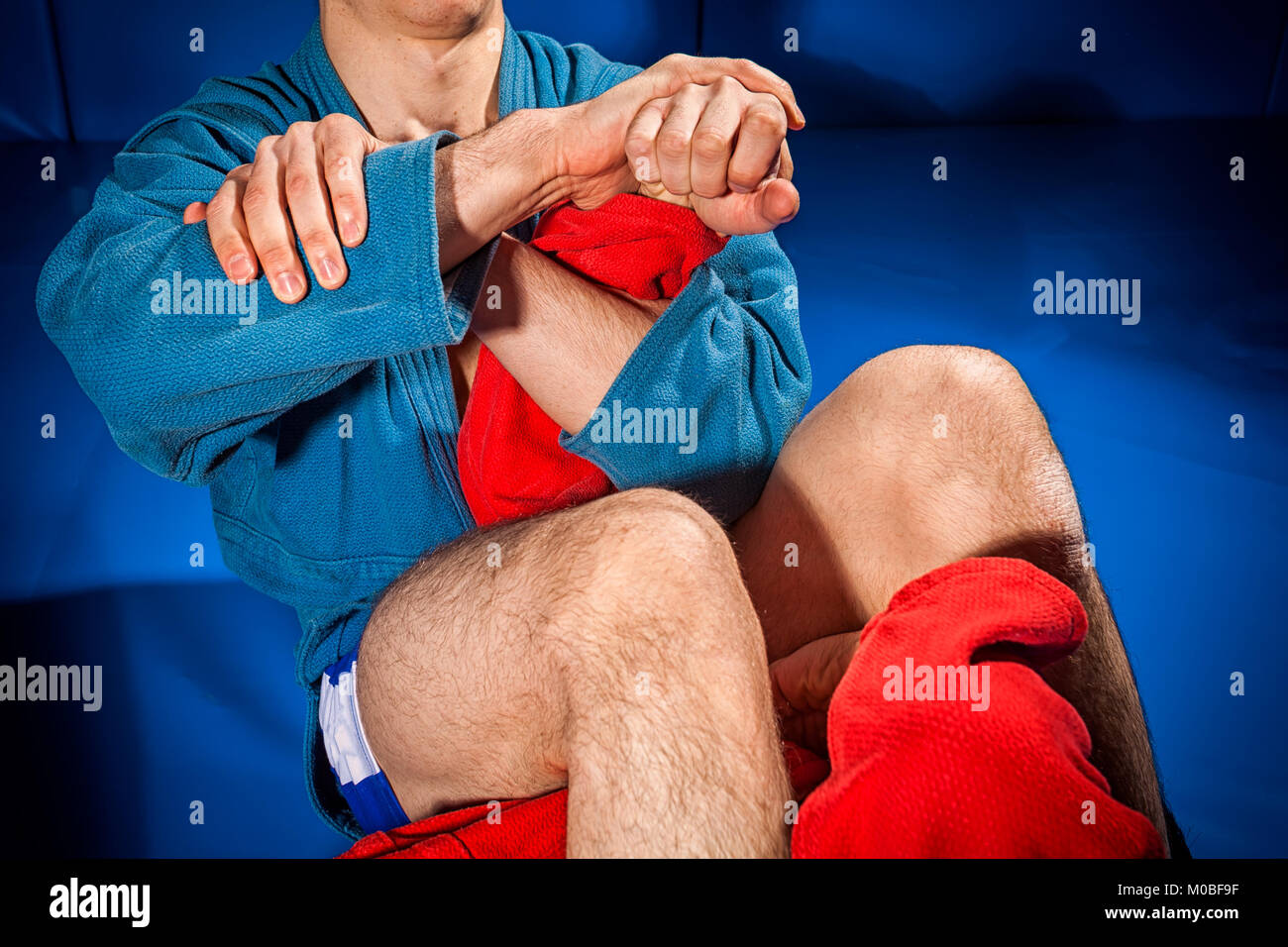 Close-up two wrestlers of grappling and jiu jitsu in a blue and red kimono makes armbar .Submission wrestling   on blue tatami Stock Photo