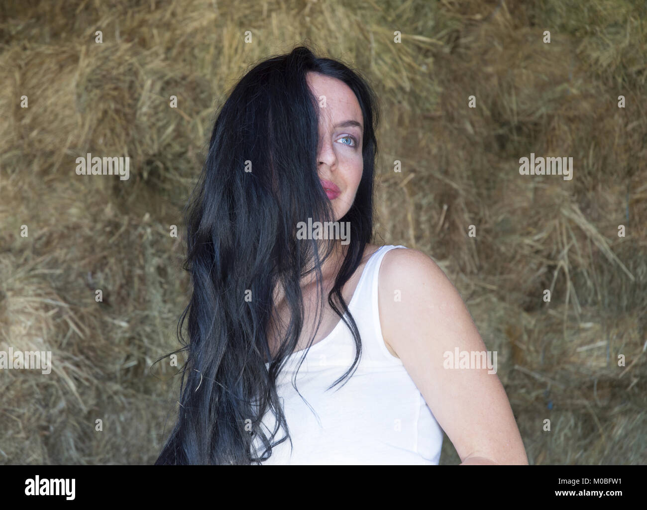 Pensive female with disheveled black hair across a half of  her face, smiling and looking at distance Stock Photo