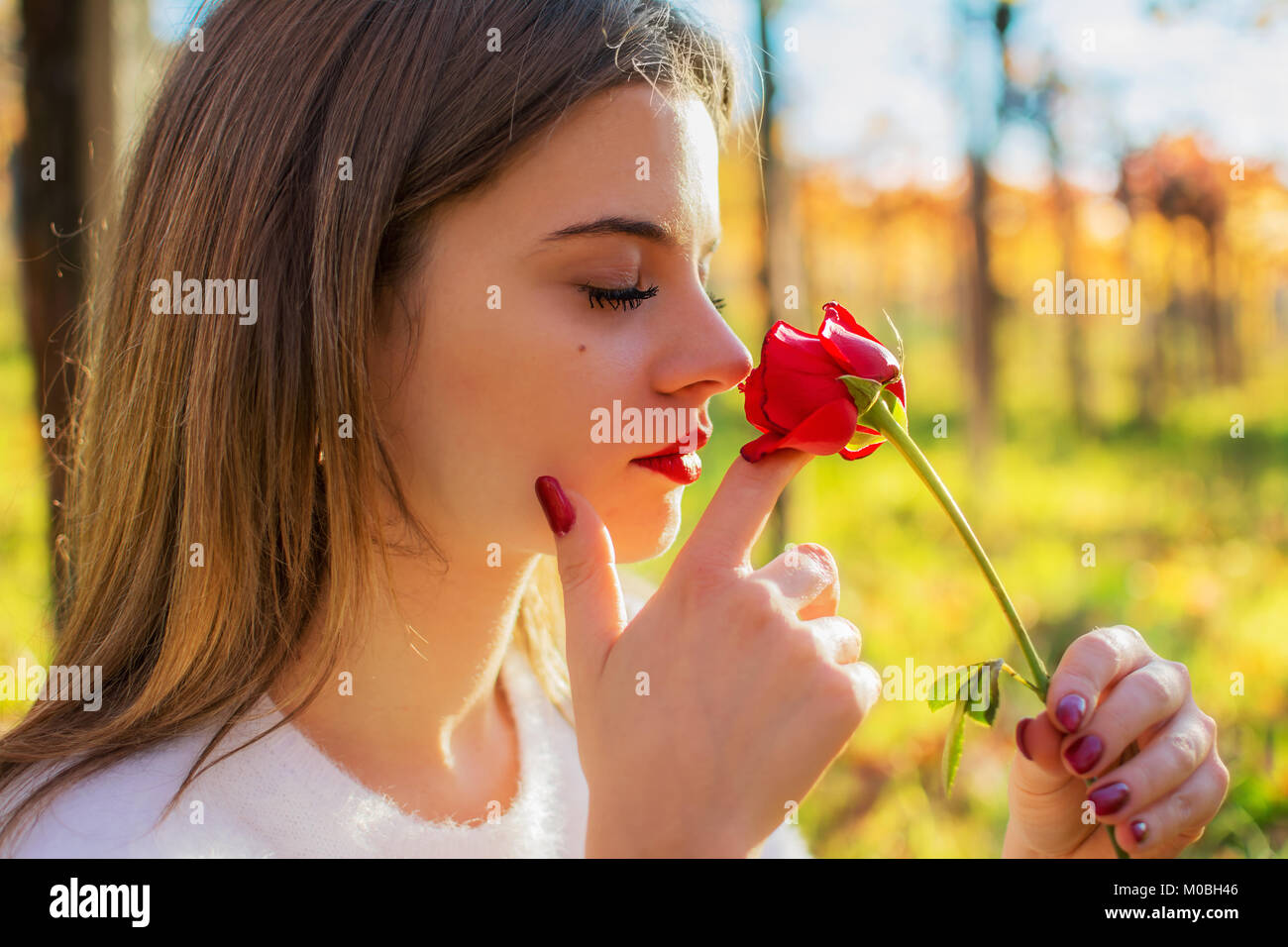 A Girl with closed eyes sniffing a red rose Stock Photo - Alamy