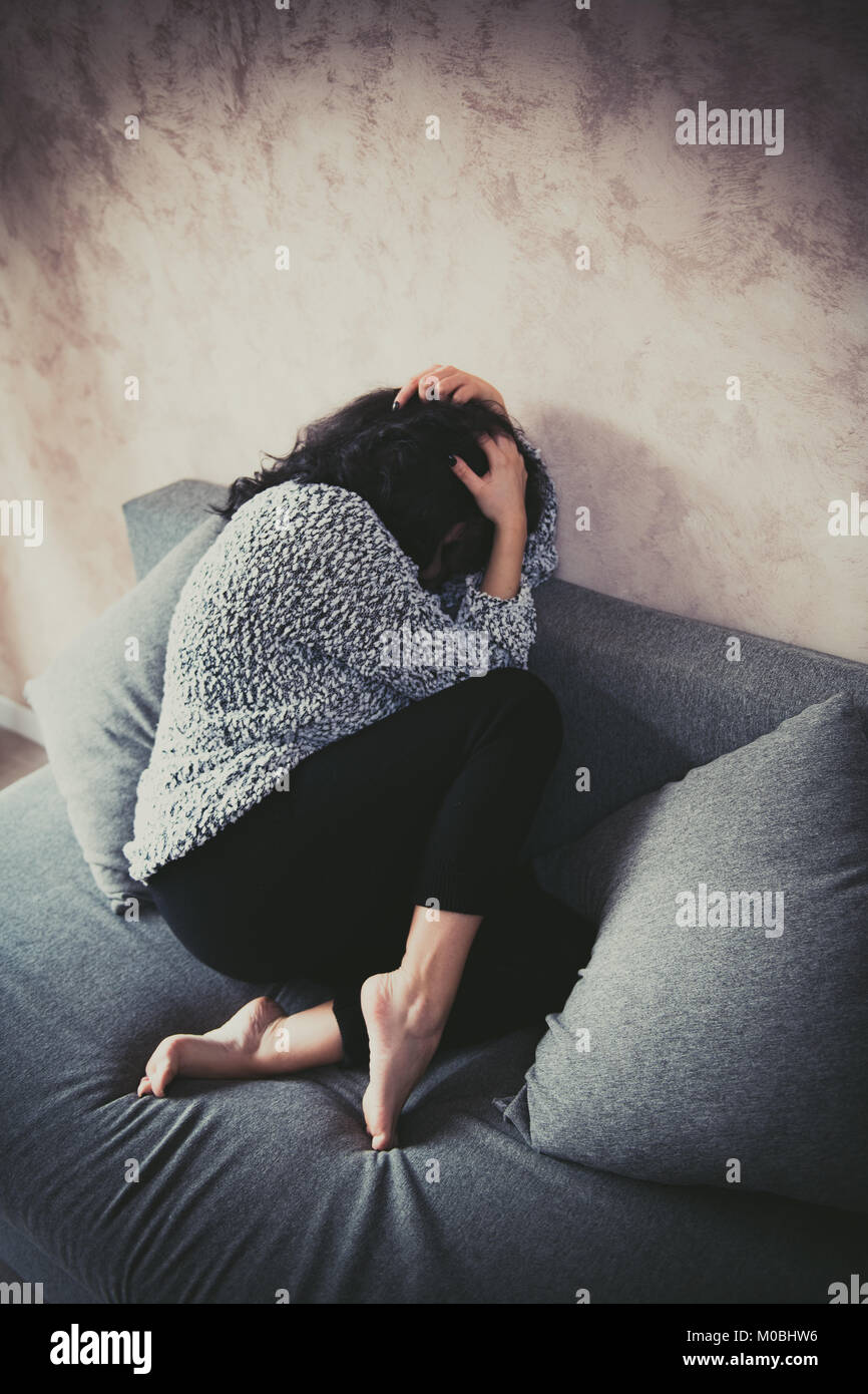 Unarmed young woman at home fetal position on sofa  protecting herself from violence and sexual harassment Stock Photo