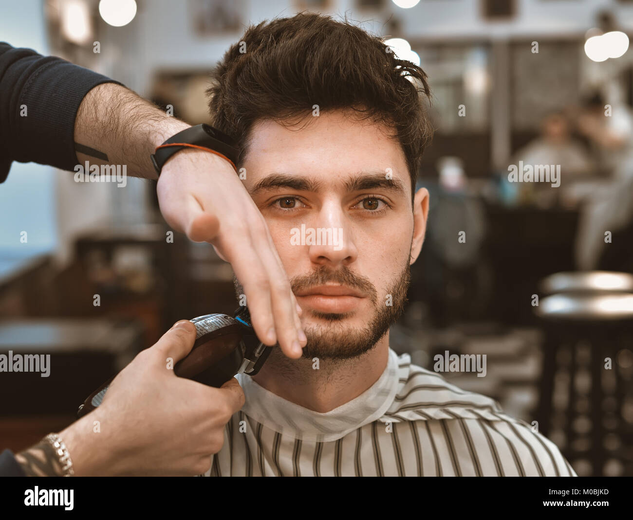 The hands of young barber making haircut to attractive man in