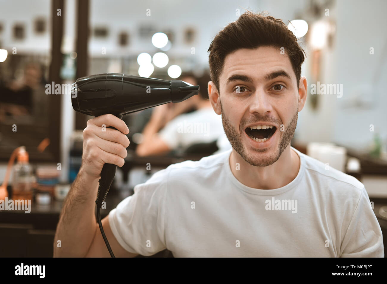 Young crazy stylish man with hair dryer and funny expressions in the