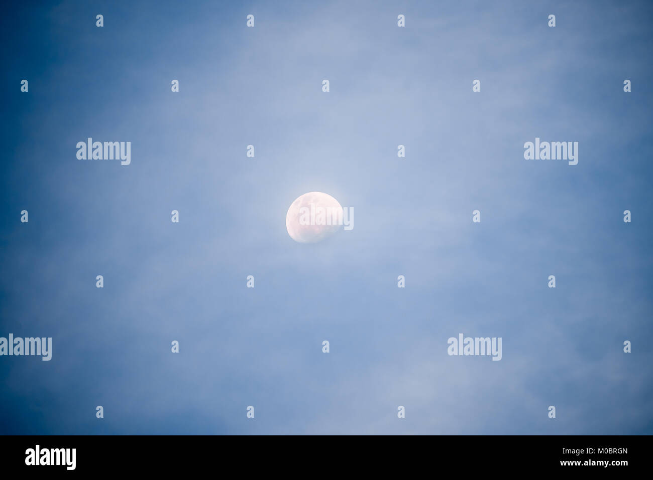 Waxing gibbous moon at night with illuminated sky and clouds Stock Photo