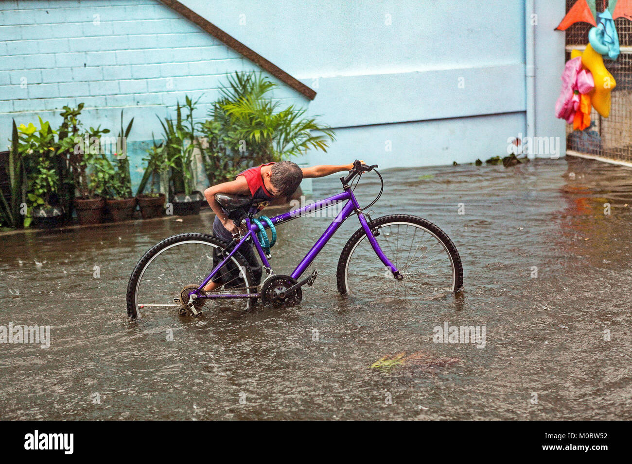 A boy pushes his bicycle through deep flood water produced by monsoon