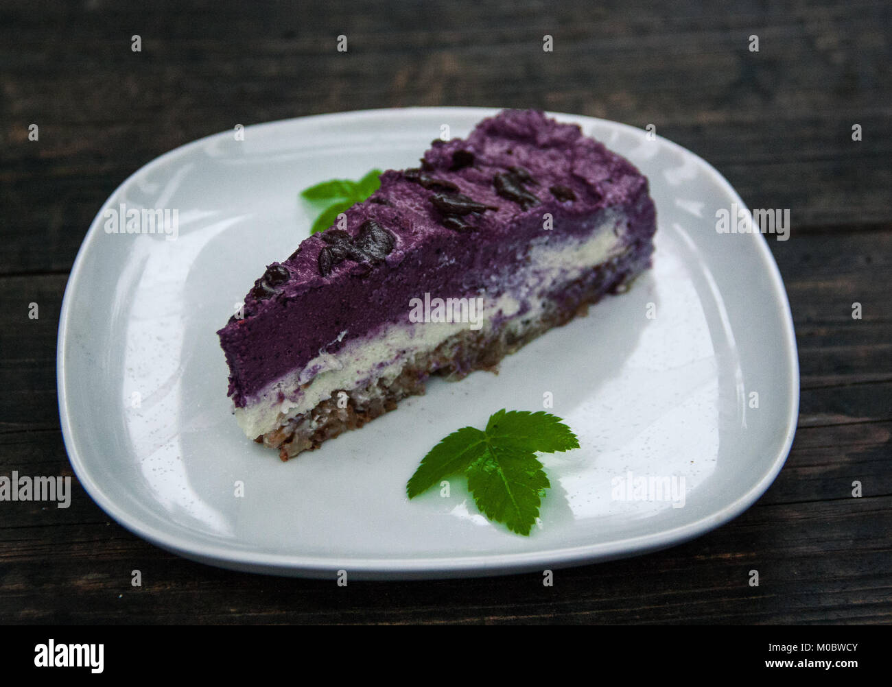 Piece of blueberry vegan pie laying on the white plate garnished with a sprig of mint Stock Photo
