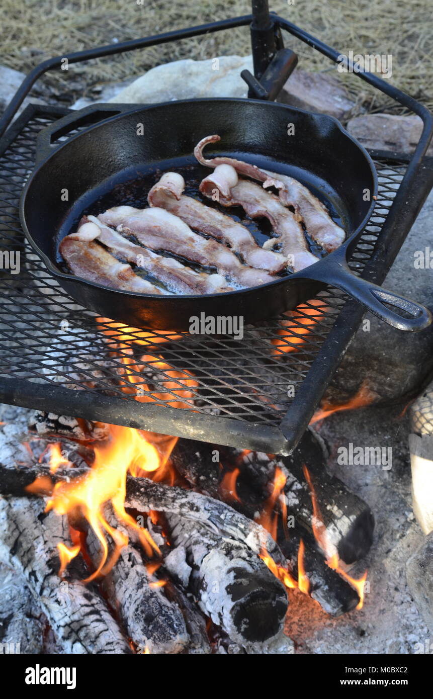 Cooking bacon over a campfire in a cast iron frying pan Stock Photo