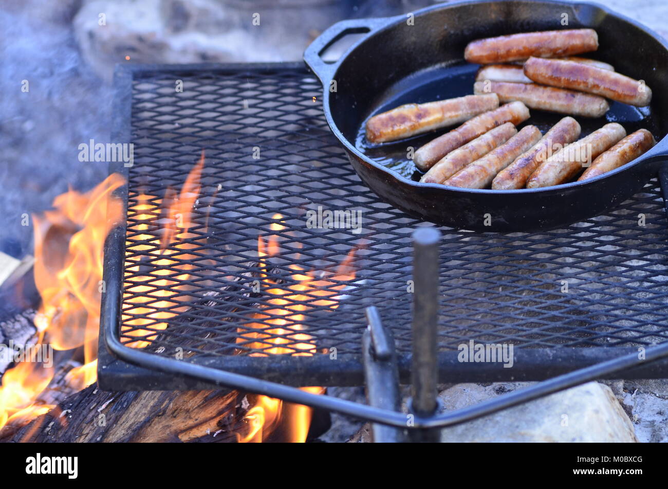 Cooking breakfast sausages over a campfire in a cast iron frying pan Stock Photo