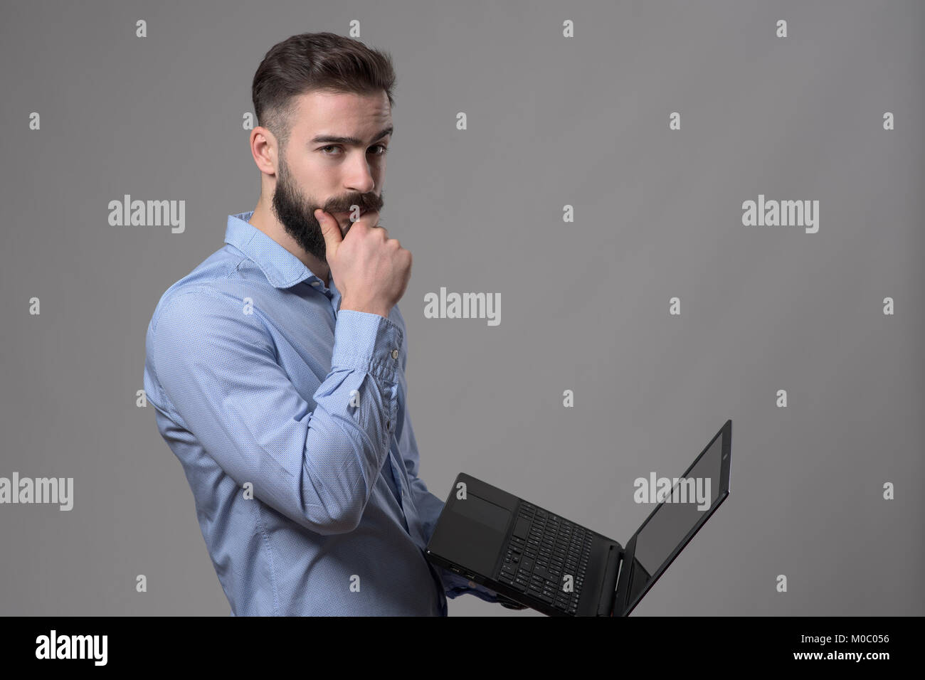 Confused young business man using laptop computer touching beard and ...