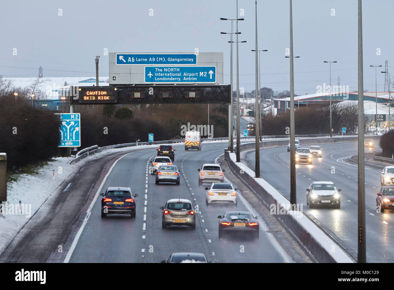 caution skid risk overhead gantry sign on motorway as cars driving along gritted salted motorway in newtownabbey northern ireland Stock Photo