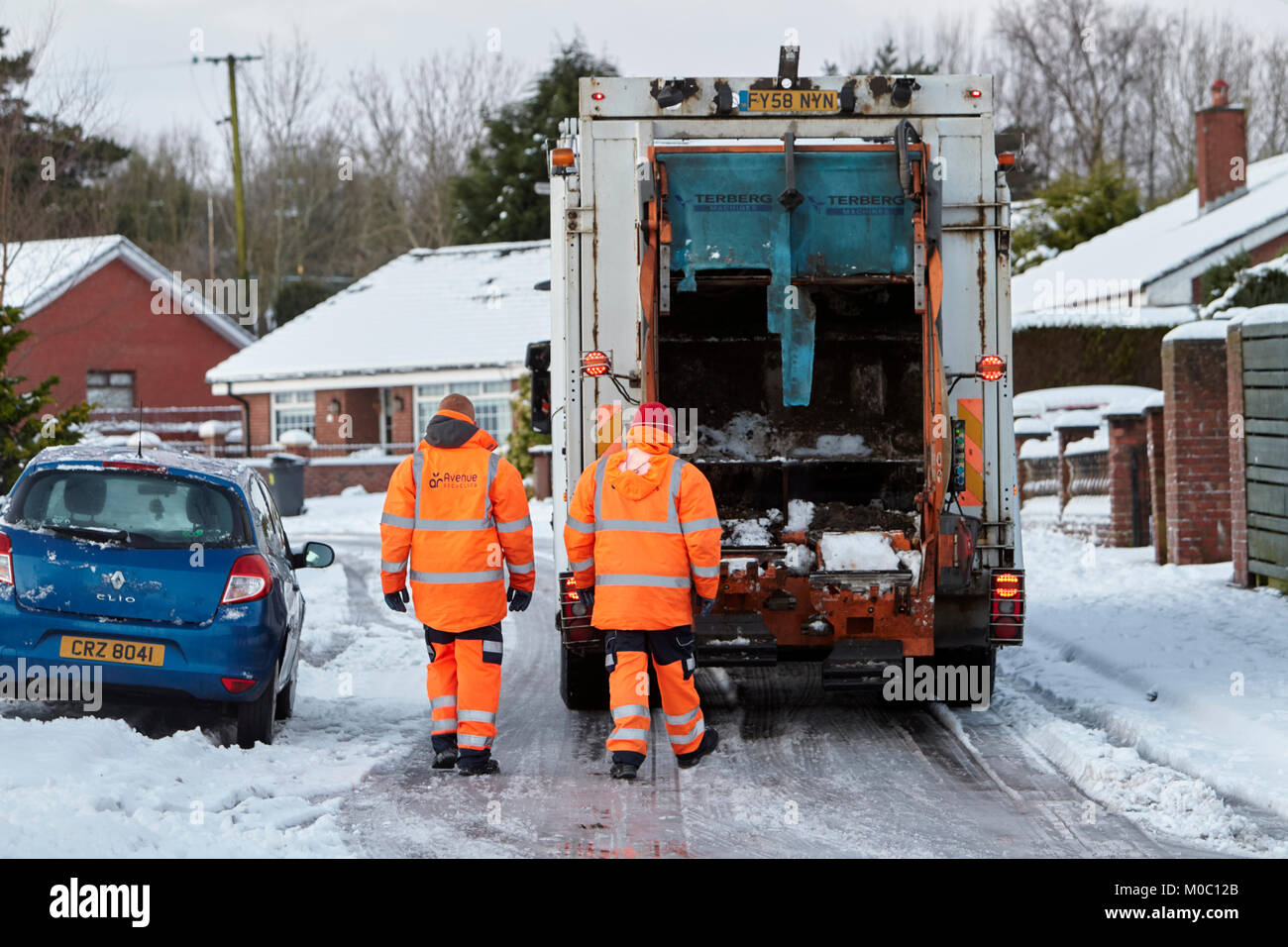 workers with refuse recycling collection truck driving along street covered in snow in newtownabbey northern ireland Stock Photo