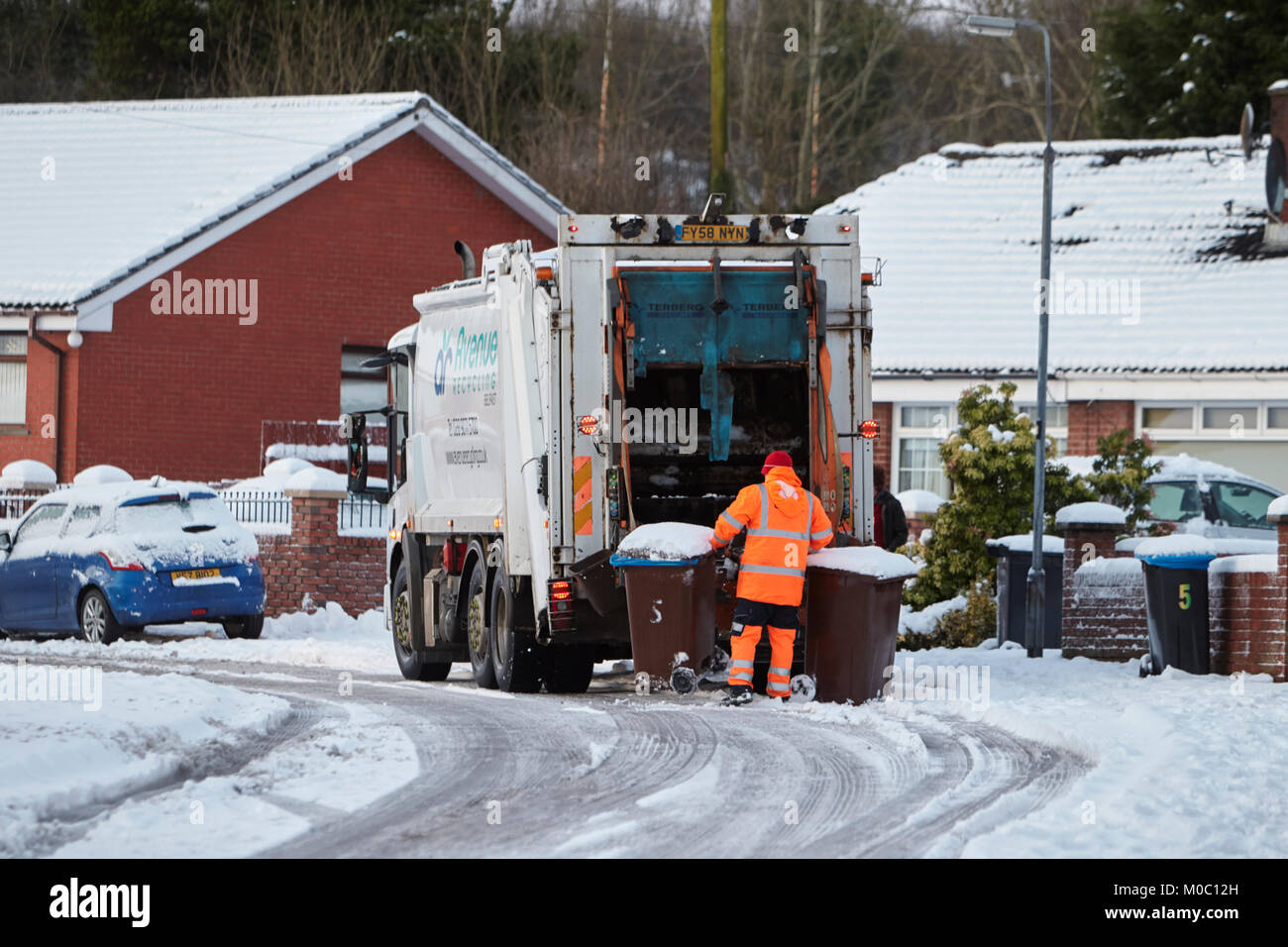 worker collecting bins with refuse recycling collection truck driving along street covered in snow in newtownabbey northern ireland Stock Photo
