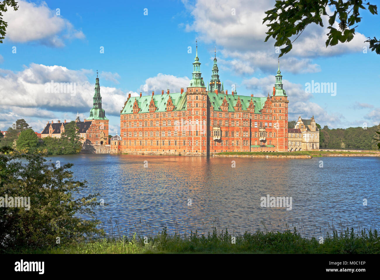 The Frederiksborg Castle in Dutch Renaissance style in Hillerød, North Sealand, Denmark, in bright summer morning sunshine seen through spring leaves. Stock Photo