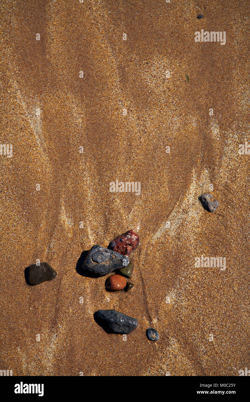 Small colorful stones on a beach with water runoff patterns in the sand Stock Photo