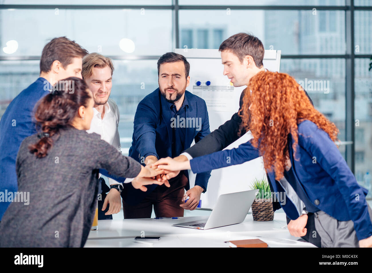 business team is giving high five and smiling while standing in office ...