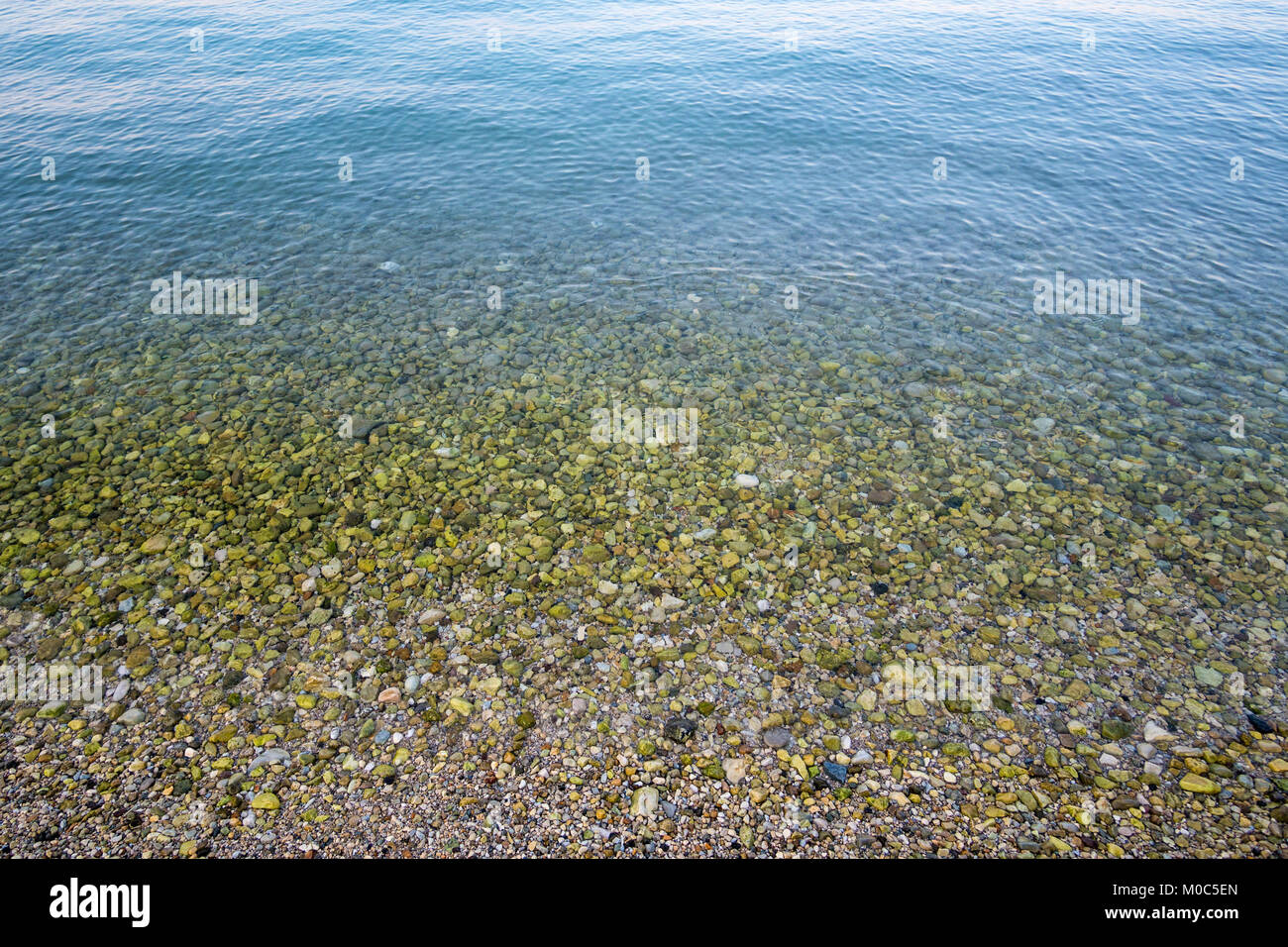 Sea surface and gravel beach full of green stones in shallow water Stock Photo