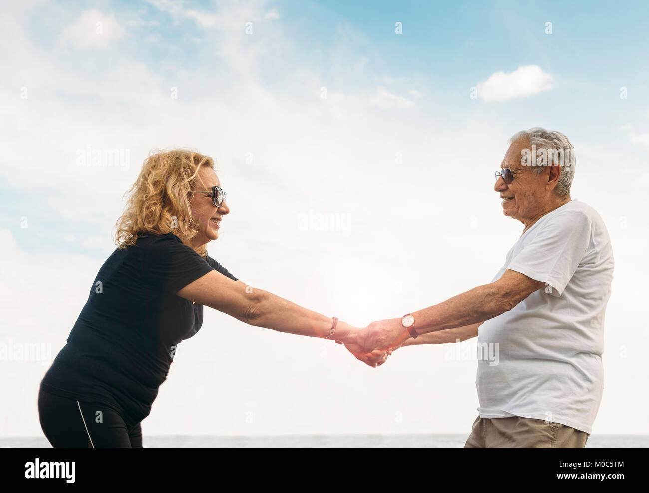 Model Released:  Mature heterosexual couple stretching together against blue sky outdoors Stock Photo