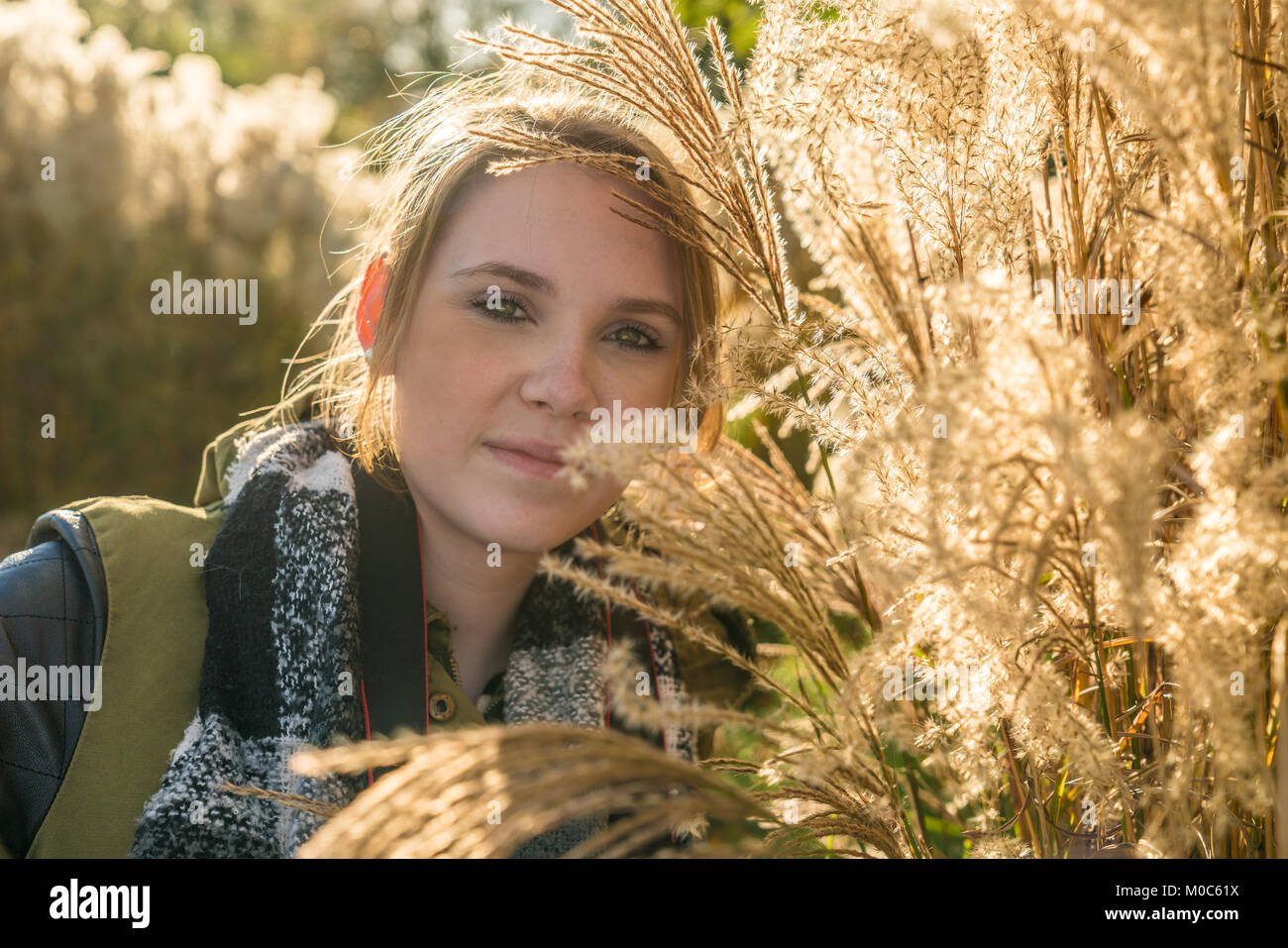 Young woman looks into camera and stands among bushes in park Stock Photo