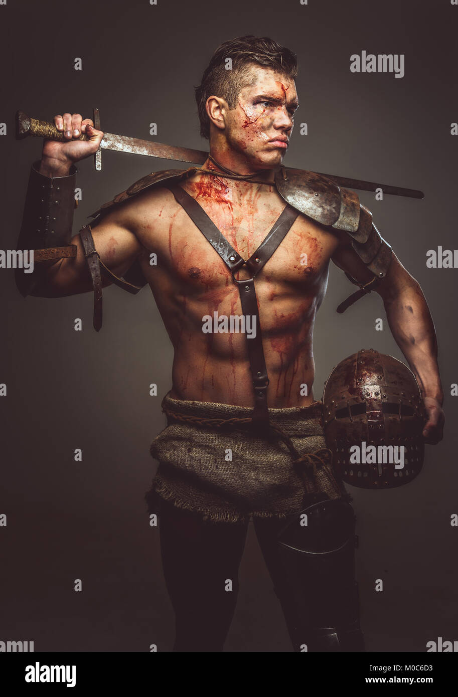 Muscular shirtless gladiator holding helmet and sword Stock Photo - Alamy