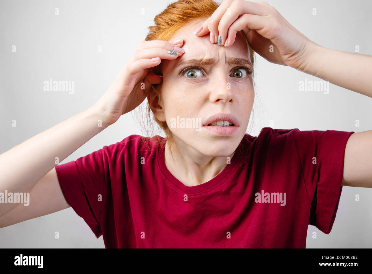 redhead woman squeezing her pimples, removing pimple from her face Stock Photo