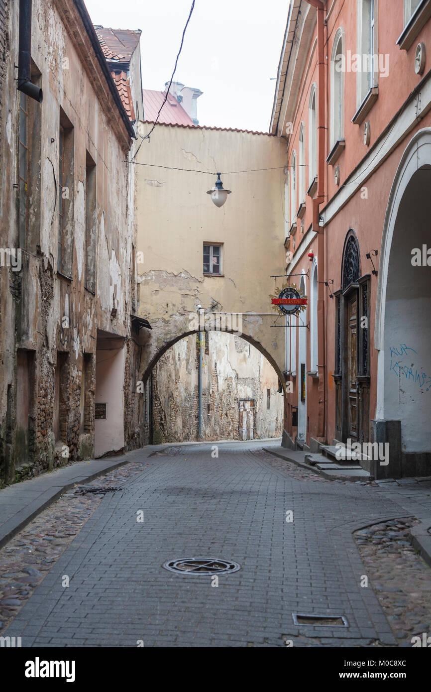 The narrow Sv Kazimiero Gatve with old dilapidated arch built over the road in the Old Town of Vilnius, capital city of Lithuania, and bar sign Stock Photo