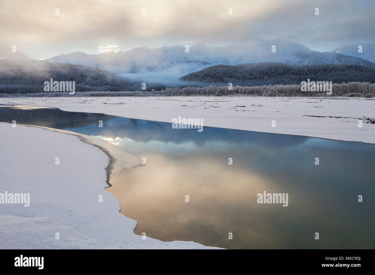 Fog decending on the Chilkat river at sunset with reflections on open water in winter. Stock Photo