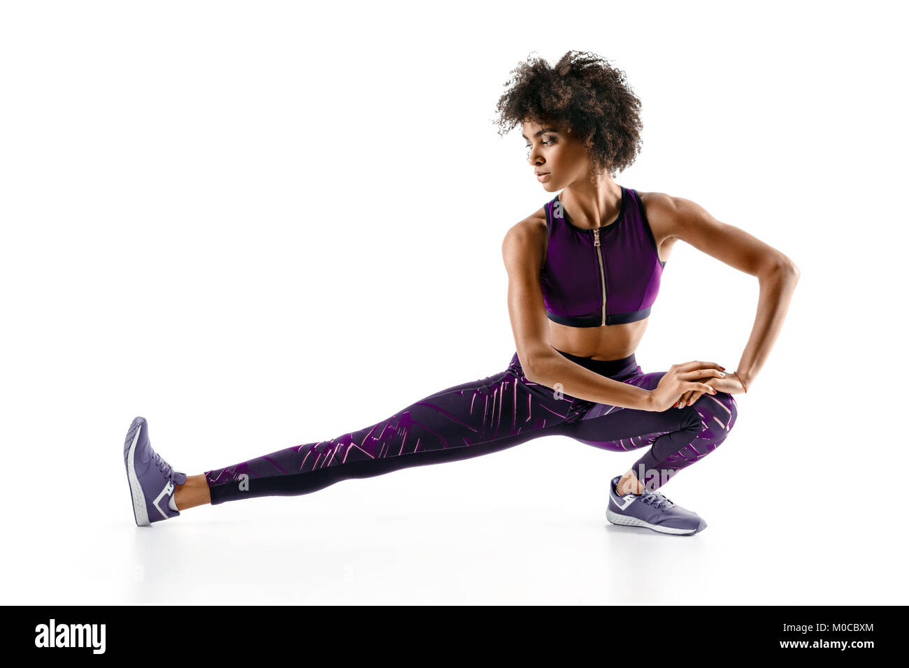 Athlete girl stretching her hamstrings. Photo of young african girl doing exercising on white background. Sports Stock Photo