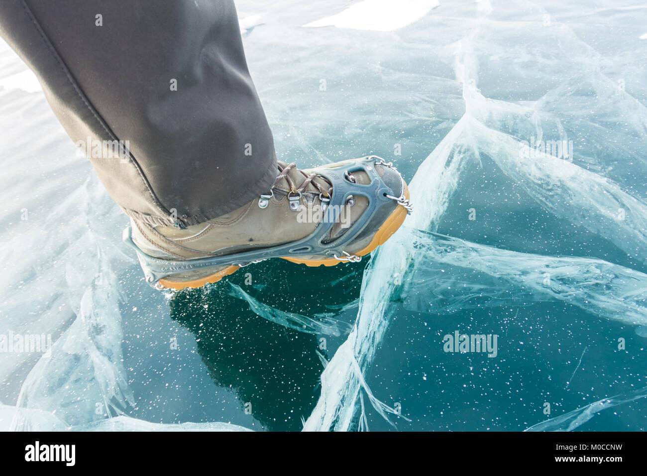 Human legs in hiking boot in ice crampons on the texture Baikal ice