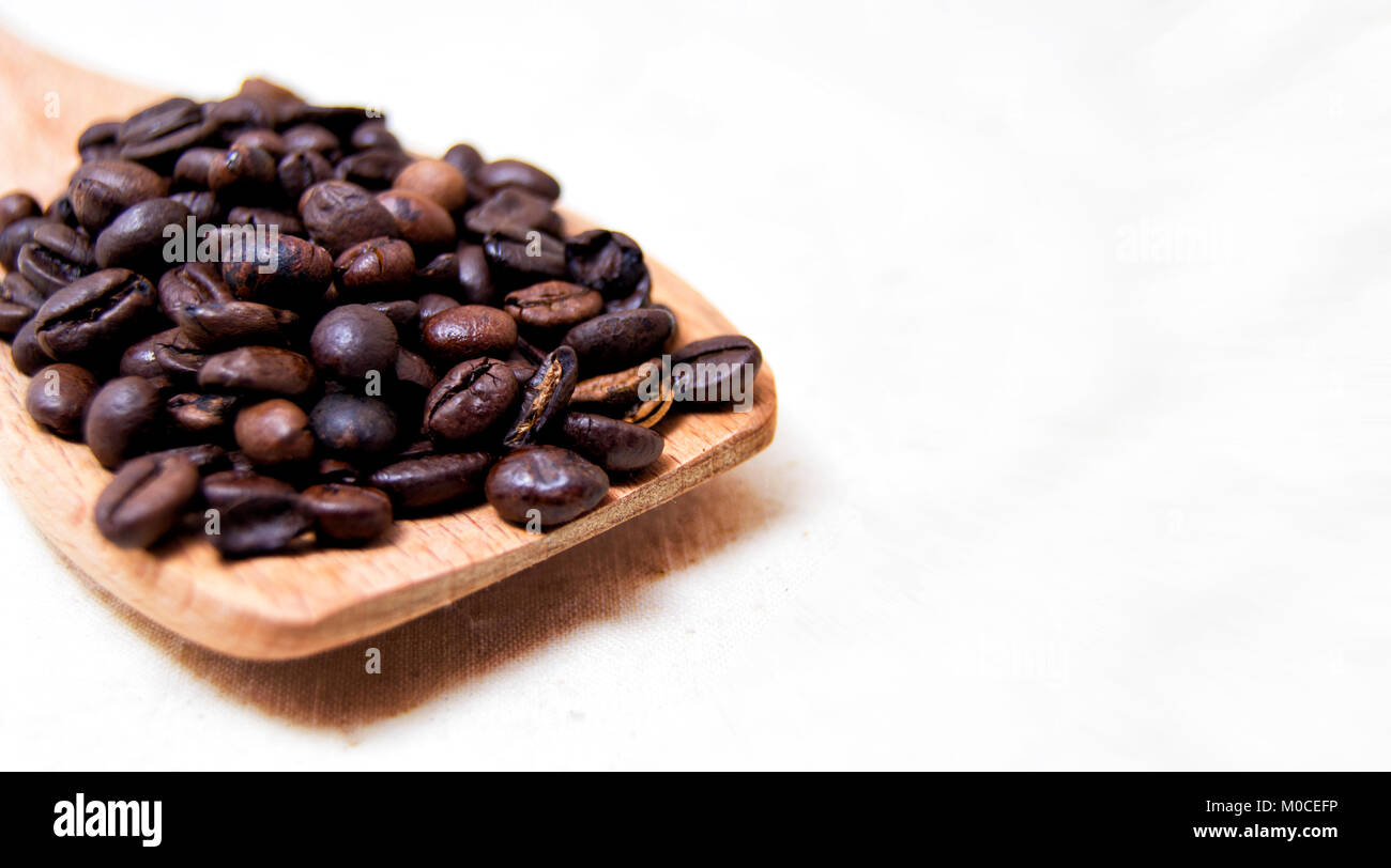 close up of roasted coffee beans on a wood spoon with white background ...