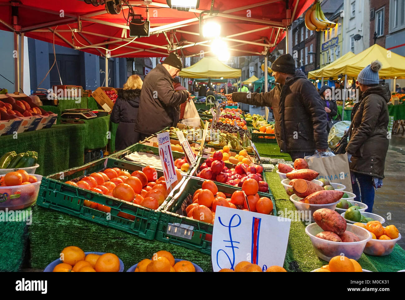 A market stall vendor on a fruit and veg stall makes a sale at Surrey Street market in Croydon, South London. Stock Photo