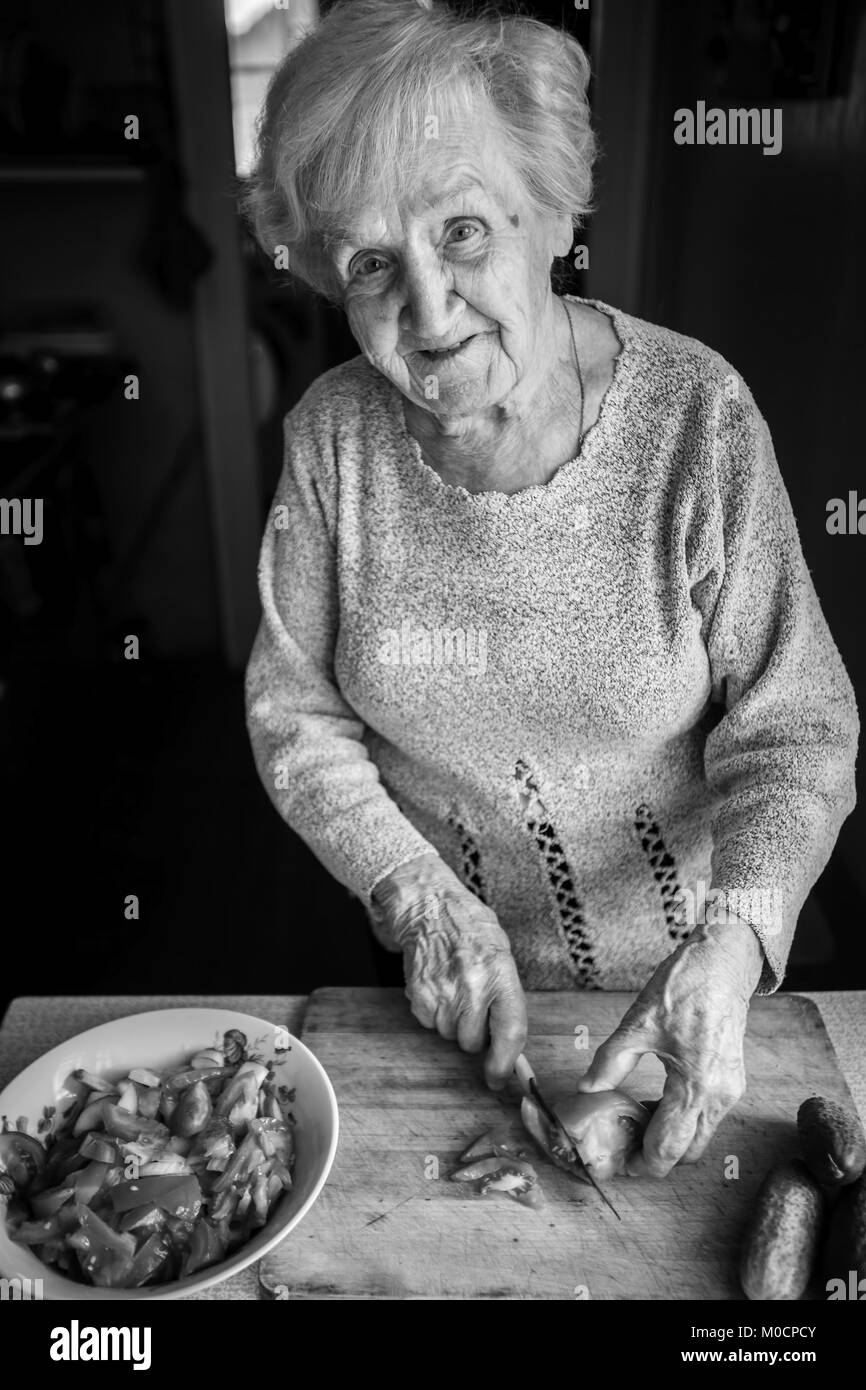 An elderly woman chops tomatoes for a salad. Black and white photo. Stock Photo
