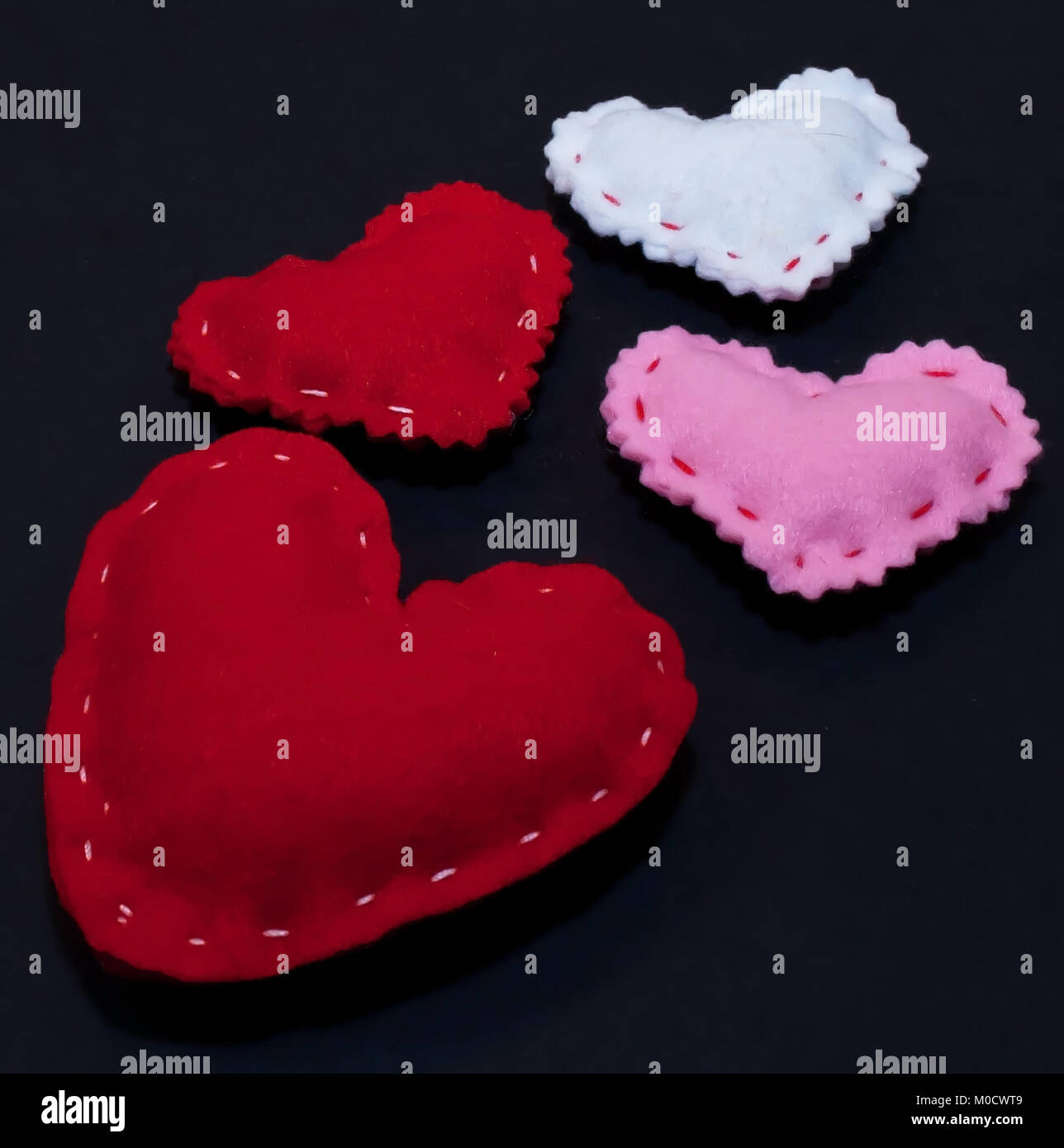 Four hearts, three smaller ones, red, white and pink along with a larger red one on a black background Stock Photo