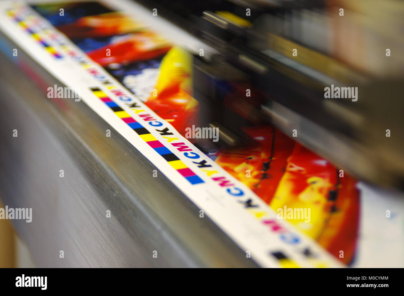 Inkjet plotter printing head moving over CMYK mark on white paper. Large digital printer machine. Stock Photo