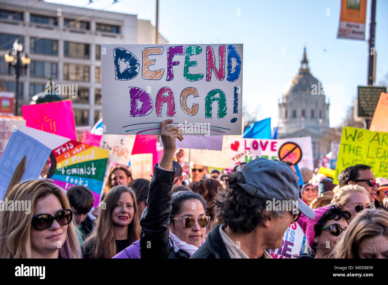 San Francisco, California, USA. 20th January, 2018. The 2018 Women's March in San Francisco, organized by Women's March Bay Area. As the crowd marches down Market Street with City Hall in the background, a woman holds a sign high reading, 'Defend Daca!' Stock Photo
