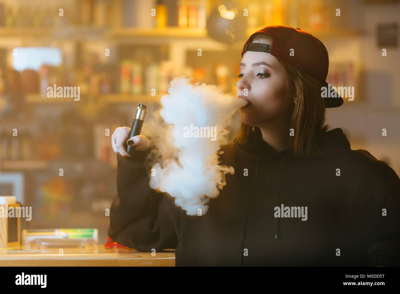 Young pretty woman in red cap smoke an electronic cigarette at the vape  shop. Hip-hop style. Closeup Stock Photo - Alamy