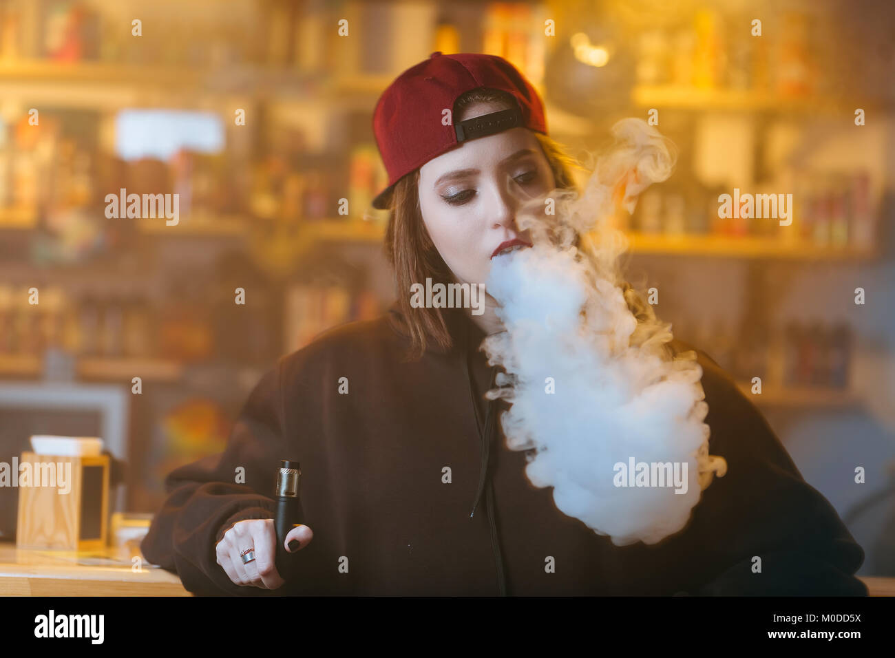 elfbar nachfüll pod läuft aus Young pretty woman in red cap smoke an electronic cigarette at the vape  shop. Hip-hop style. Closeup Stock Photo