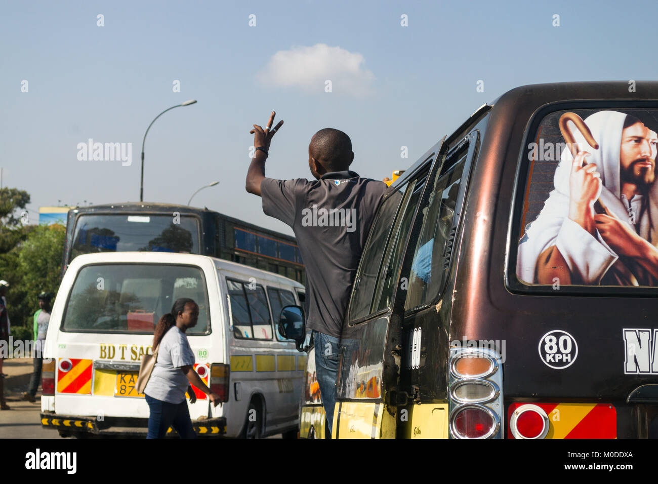 A bus driving on a road with the conductor standing in the doorway waiting for passengers, Nairobi, Kenya Stock Photo