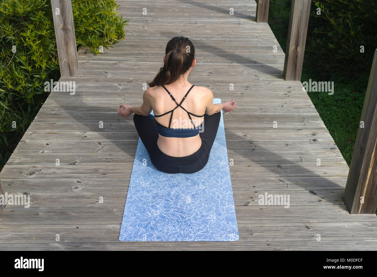 woman practicing yoga on a mat outside on a wooden boardwalk, crossed legged lotus pose. Stock Photo