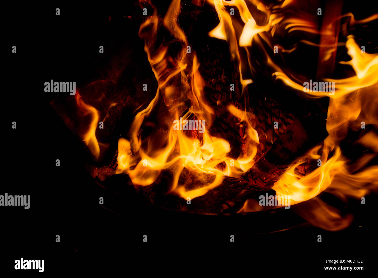 A close up of hot burning embers and charred logs surrounded by flames ...