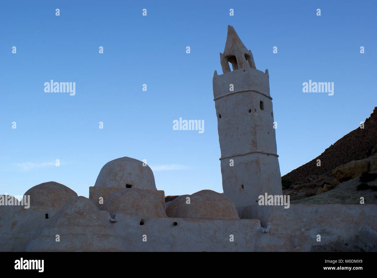 White stone Mosque of the Seven Sleepers silhouetted against the sky at dusk, Chenini, Tataouine district, Tunisia Stock Photo
