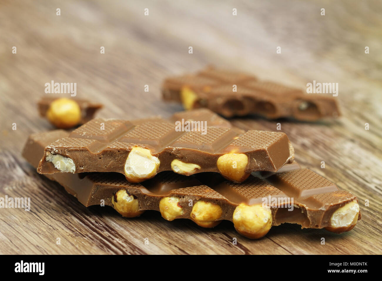Pieces of milk chocolate with whole hazelnuts on wooden surface Stock Photo