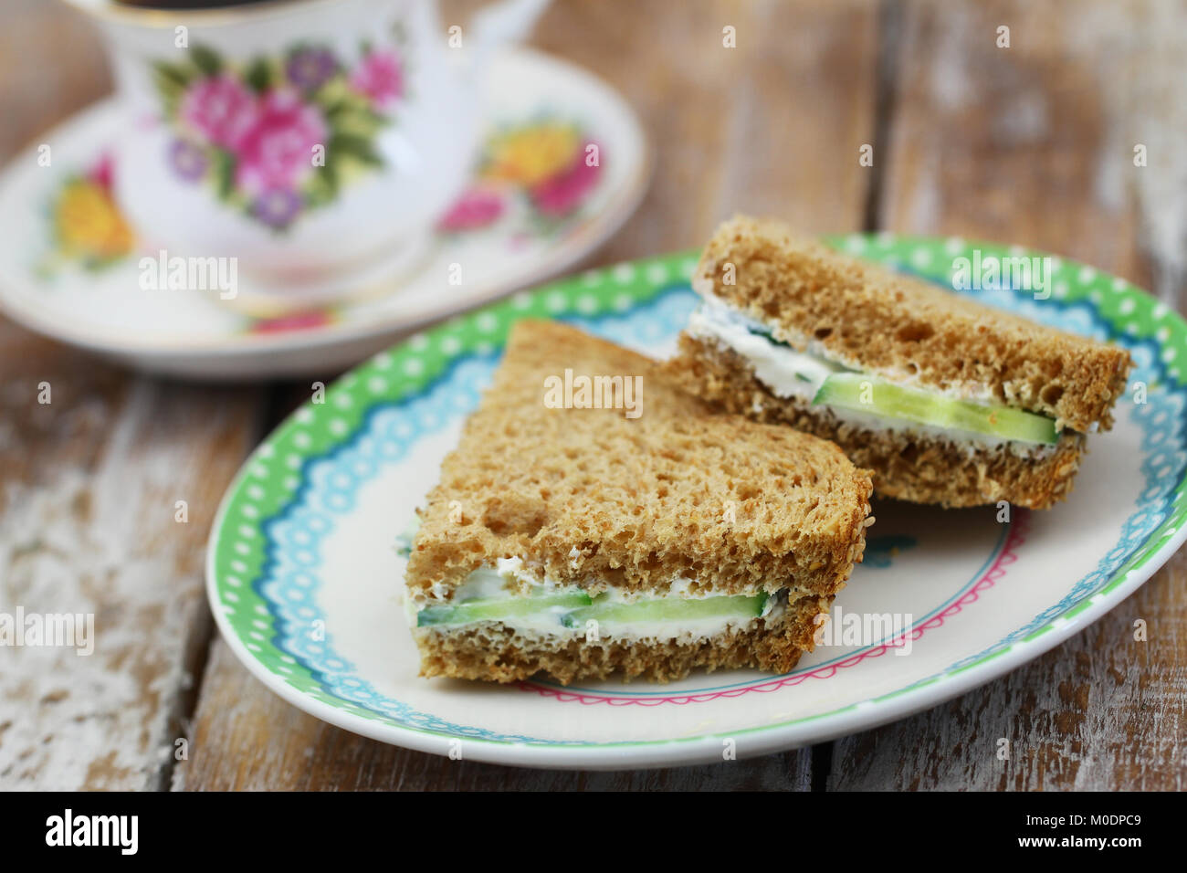 Brown bread sandwiches with cream cheese on plate with cup of tea in