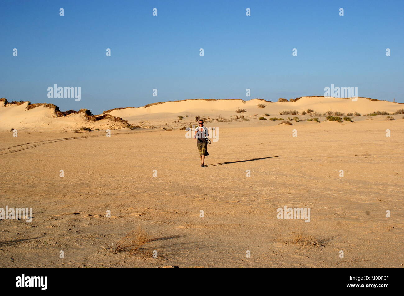 Lady walking away from sand dunes near Douz, Sahara desert, Kebili district, Tunisia Stock Photo