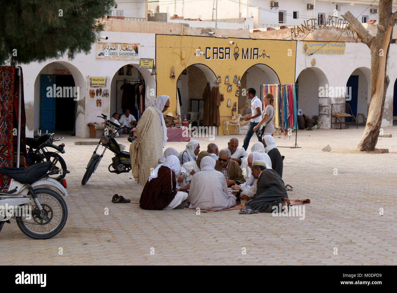 Group of Tunisian men sitting on the ground in Douz centre square, Douz, Kebili district, Tunisia Stock Photo