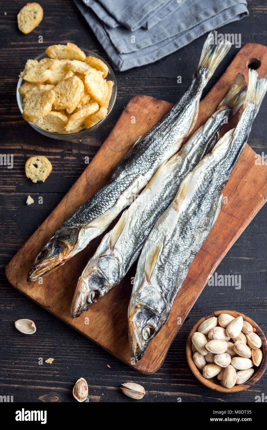Assorted snacks for beer: sun dried fish, nuts, salted croutons or crackers over wooden background, top view, copy space. Lager beer and snacks, dried Stock Photo
