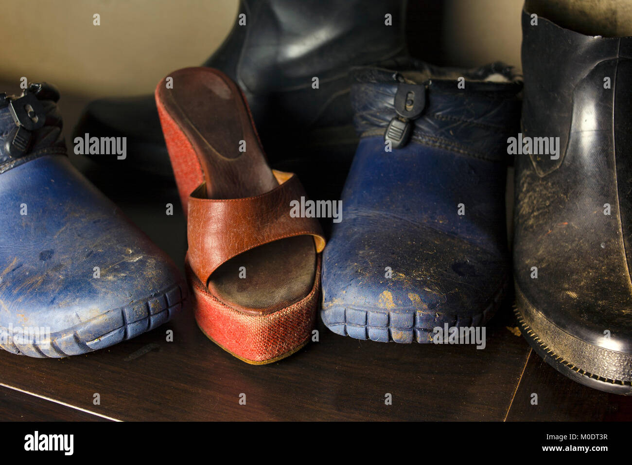 Dirty boots and shoes closeup with a red high heel in the center of composition, studio shot Stock Photo