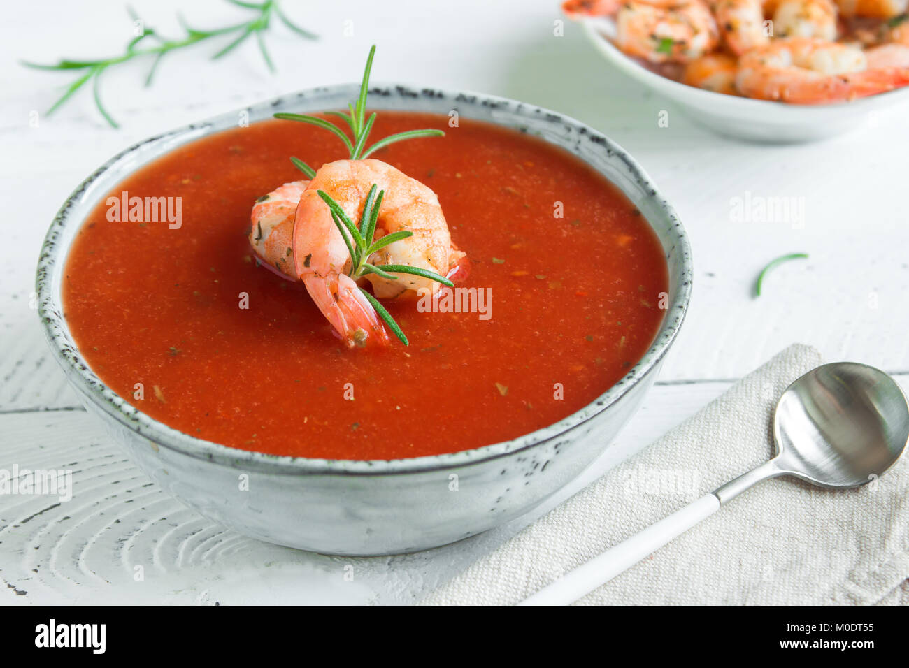 Vegetable tomato soup gazpacho with shrimps (prawns) and rosemary in bowl on white wooden background, top view, copy space. Stock Photo