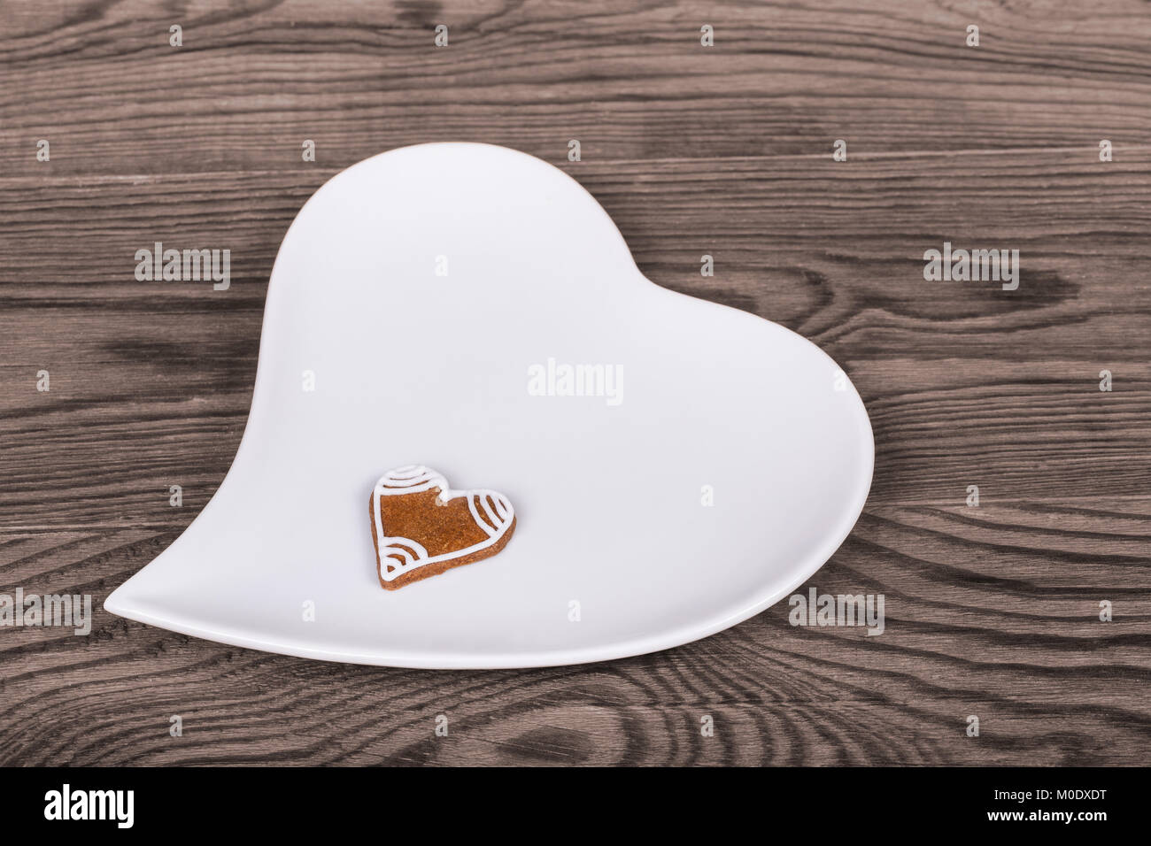 Valentine's hearts for good luck, hand-decorated gingerbread and white plate. Symbols of love, bond, marriage or friendship on a brown wood background. Stock Photo