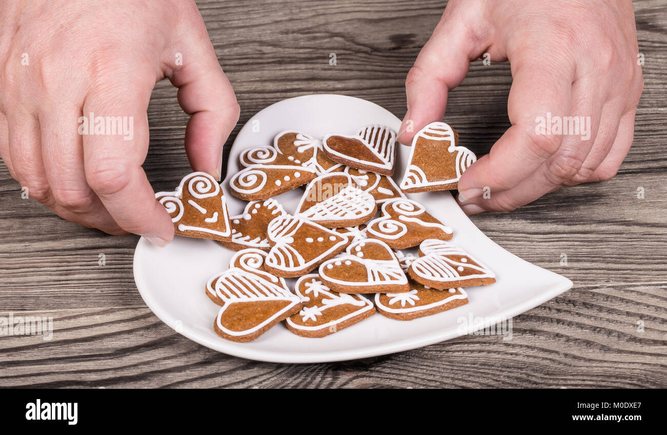 Female hands and sweet gingerbreads for good luck. Decorative cookies and plate in heart shape on a wood table. Love, bond, marriage or friendship. Stock Photo