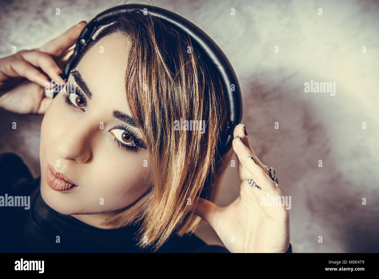 Young beautiful blond girl with headphones portrait face close up listening music looking at camera Stock Photo